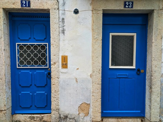 zwei leuchtend blaue Haustüren nebeneinander.nDie Fenster in den Türen sind unterschiedlich breit und hoch. Das linke Fenster ist vergittert