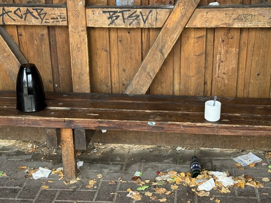 Wartehäuschen aus Holz an einem Bahnhof. Auf einer Sitzbank wurden Kanne und Kaffeepott zurückgelassen.