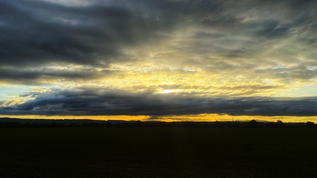 Die Abendsonne geht hinter einem Wolkenband unter und strahlt zwischen den Wolken durch.