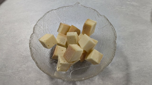 A glass bowl filled with small, cubed pieces of yellowish cheese, some with a slightly darker edge. The bowl has a decorative leaf pattern.