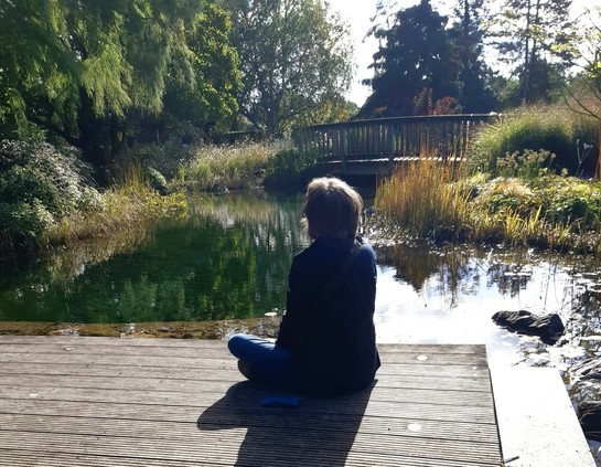 Frau sitzt auf einem Holzdeck an einem Teich