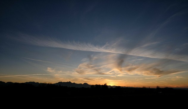 dunkles unteres Drittel und drüber beginnender Sonnenuntergang mit Kondensstreifen und wenigen Wolken am eher blauen Himmel 