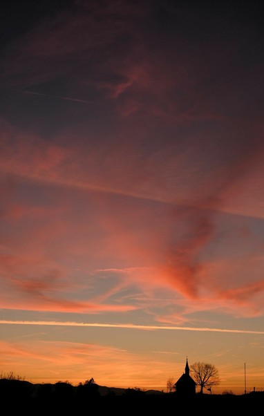 Silhouette einer Kapelle unter farbig rötlich orange bunten Wolken 