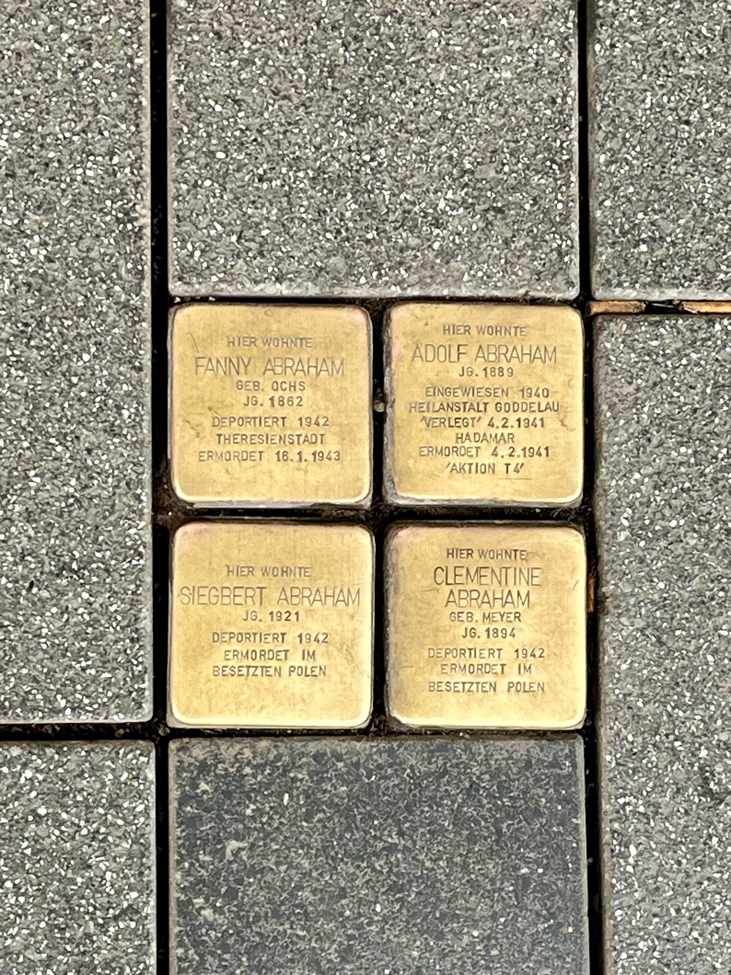 Vier goldene zu eine Quadrat angeordnete Stolpersteine in grauen Pflaster Vier goldene zu eine Quadrat angeordnete Stolpersteine in grauen Pflaster