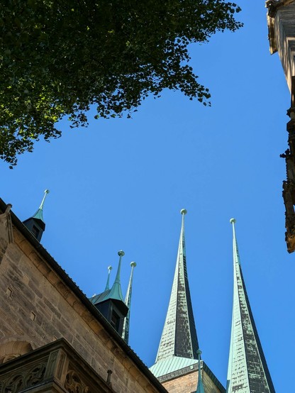 von unten an einer Kirche in den blauen Himmel fotografiert.n6 spitze Turmspitzen mit kleinen Kugeln drauf und grünlichem Kupferspan sind zu sehen 