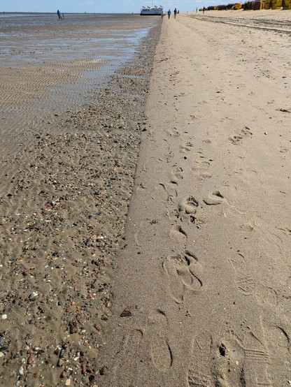 eine grade Linie am Strand. Links welliger flacher Sand, rechts ansteigend