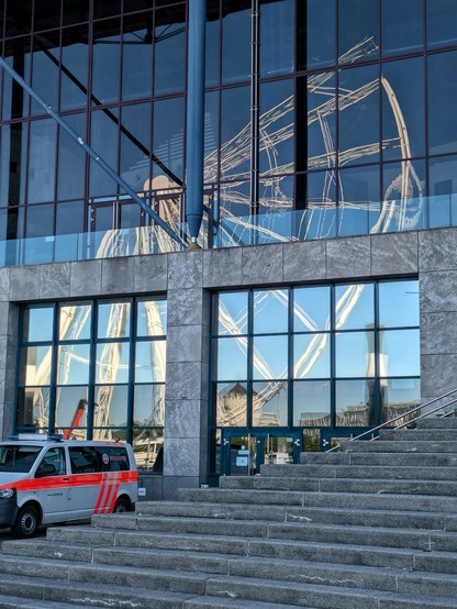 ein zu zwei Dritteln abgebautes Riesenrad spiegelt sich in einer großen Glasfläche 