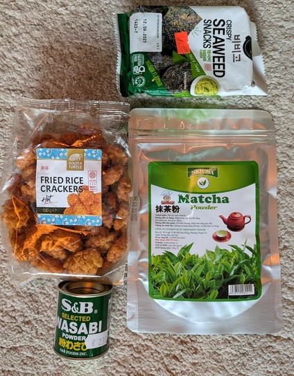 auf einem hellen Teppich liegen nPackungen mit Algensnack, Matcha und Reiscrackern und eine Dose mit Wasabipulver