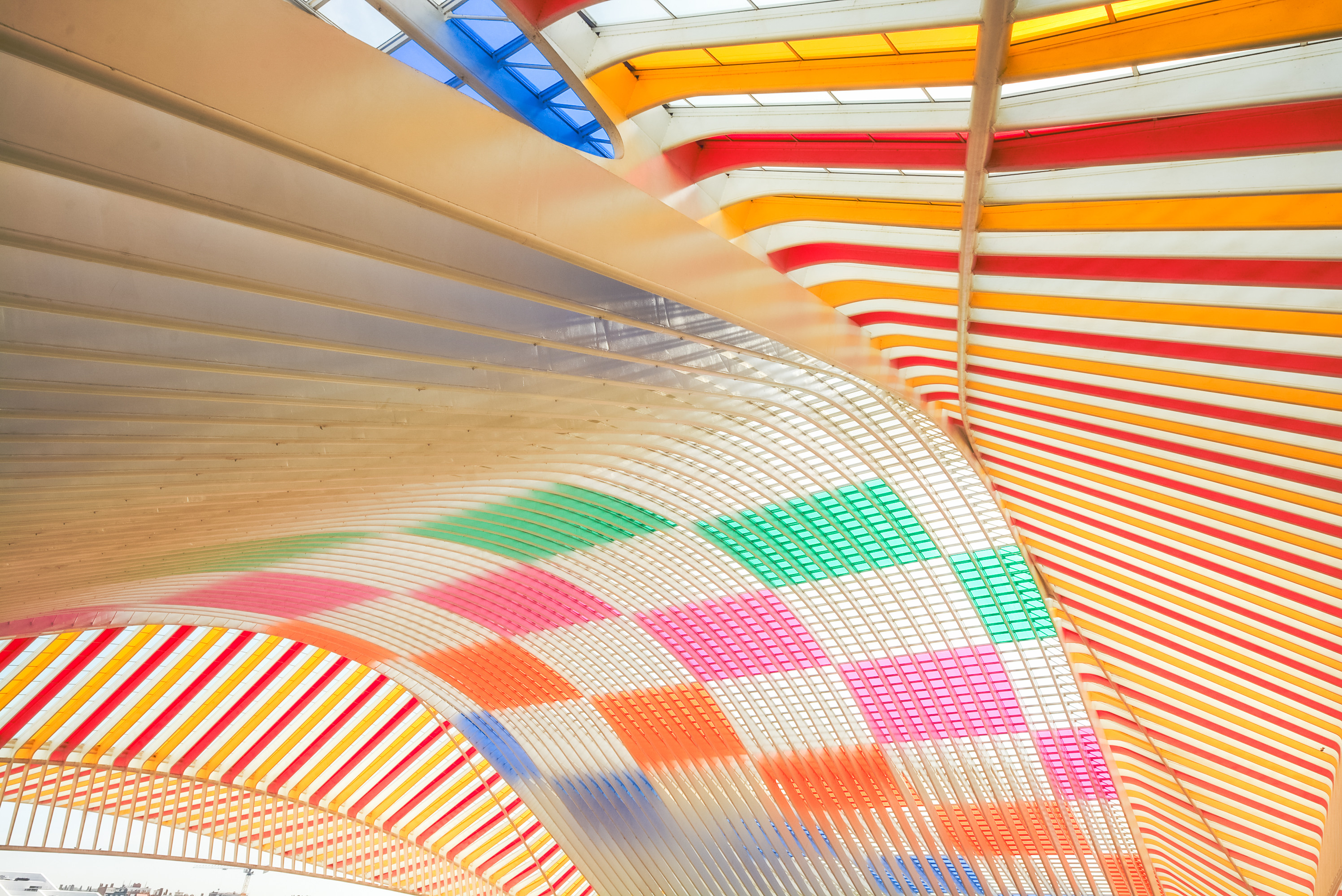 Das Bild zeigt einen farbenfrohen und dynamischen Bogen aus welligen, bogenförmigen Dachstrukturen in Rot, Orange, Gelb, Grün und Blau.
Detaillierte Beschreibung:
Das Bild zeigt eine Innenansicht einer Architektur, die durch ihre auffällige, farbenfrohe Gestaltung beeindruckt. Der Fokus liegt auf einer gewölbten Dachstruktur, die aus mehreren parallelen, wellenförmigen Elementen besteht. Diese Elemente sind in verschiedenen Farben gestrichen – hauptsächlich Rot, Orange, Gelb, Grün und Blau – und schaffen ein lebendiges, fast psychedelisches Muster. Die Farben sind kräftig und satt, wobei die Farbabstufungen harmonisch wirken. Die einzelnen Elemente scheinen aus Metall oder einem ähnlichen Material zu bestehen und sind so angeordnet, dass sie eine wellenförmige, fließende Bewegung suggerieren. Der Raum darunter ist hell und scheint offen zu sein. Der Eindruck ist modern und künstlerisch. Die Gesamtatmosphäre ist positiv, energiegeladen und etwas surreal, aufgrund des ungewöhnlichen und auffälligen Designs. Die Lichtverhältnisse im Bild lassen auf Tageslicht schließen, das durch das farbige Dach scheint. Es gibt keine Personen oder Tiere auf dem Bild. Der Fokus liegt ganz auf der Architektur und dem Spiel mit Farbe und Form.
Das Bild zeigt einen farbenfrohen und dynamischen Bogen aus welligen, bogenförmigen Dachstrukturen in Rot, Orange, Gelb, Grün und Blau.
Detaillierte Beschreibung:
Das Bild zeigt eine Innenansicht einer Architektur, die durch ihre auffällige, farbenfrohe Gestaltung beeindruckt. Der Fokus liegt auf einer gewölbten Dachstruktur, die aus mehreren parallelen, wellenförmigen Elementen besteht. Diese Elemente sind in verschiedenen Farben gestrichen – hauptsächlich Rot, Orange, Gelb, Grün und Blau – und schaffen ein lebendiges, fast psychedelisches Muster. Die Farben sind kräftig und satt, wobei die Farbabstufungen harmonisch wirken. Die einzelnen Elemente scheinen aus Metall oder einem ähnlichen Material zu bestehen und sind so angeordnet, dass sie eine wellenförmige, fließende Bewegung suggerieren. Der Raum darunter ist hell und scheint offen zu sein. Der Eindruck ist modern und künstlerisch. Die Gesamtatmosphäre ist positiv, energiegeladen und etwas surreal, aufgrund des ungewöhnlichen und auffälligen Designs. Die Lichtverhältnisse im Bild lassen auf Tageslicht schließen, das durch das farbige Dach scheint. Es gibt keine Personen oder Tiere auf dem Bild. Der Fokus liegt ganz auf der Architektur und dem Spiel mit Farbe und Form.