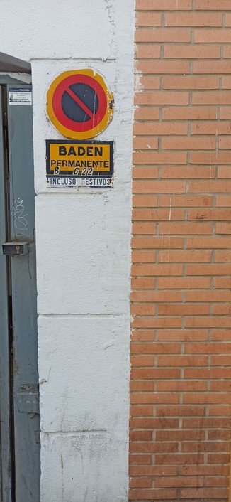 Rechter Rahmen einer Garageneinfahrt. 30 cm weiß gestrichen, dann Ziegel. Oben ein Parkenverbotsschild mit Beschriftung "Baden Permanente" inkluso Festivos