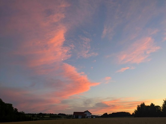 Sonnenuntergang mit rosaorangen Wolken am hellblauen Himmel, die eine kleine Mondsichel sichtbar werden lassen 