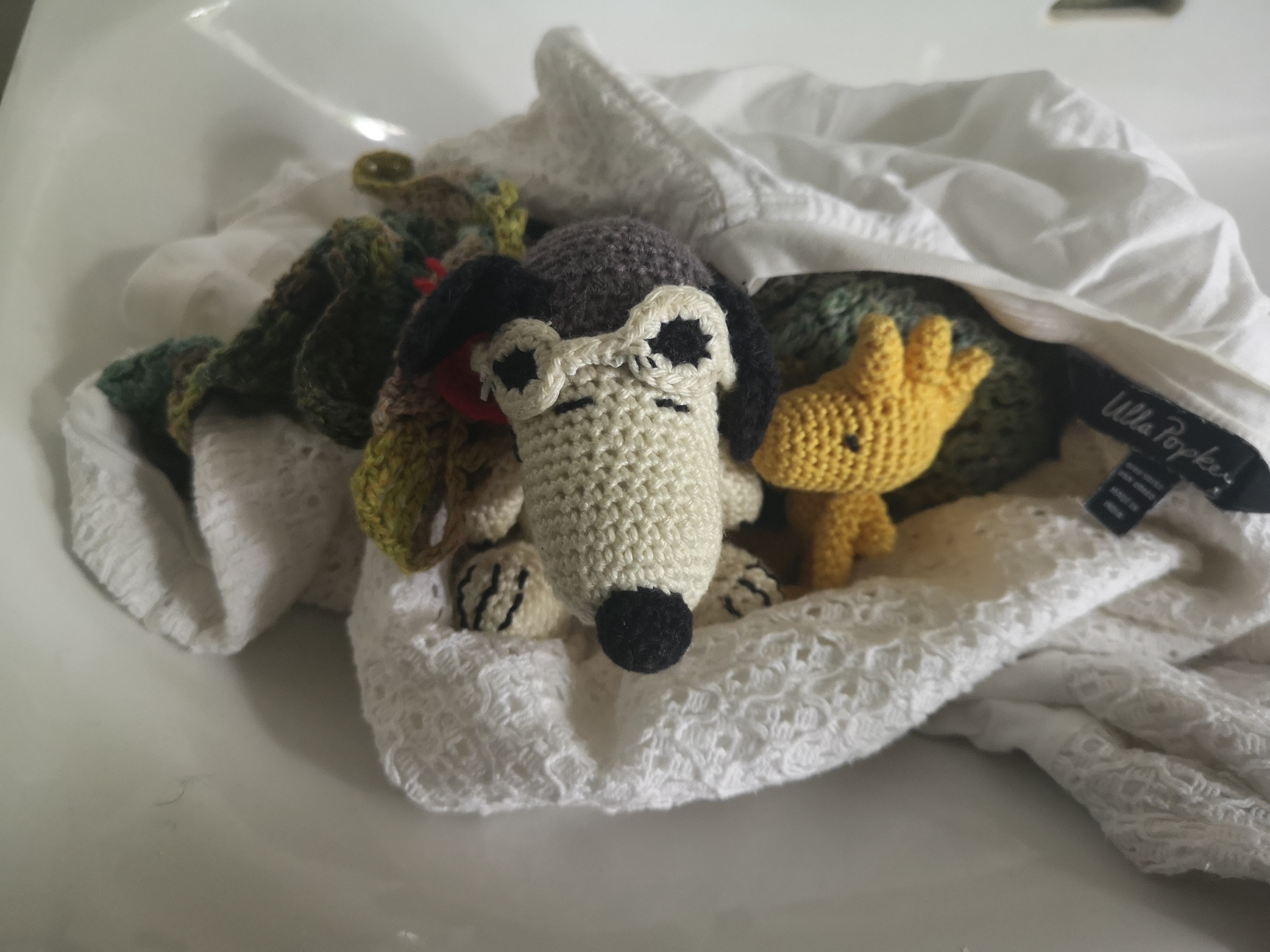 Snoopy und Woodstock (gehäkelt in Amigurumi Technik) steigen zusammen mit einem weißen Spitzen-Shirt und einem Schal in den Wäschesack. Snoopy und Woodstock (gehäkelt in Amigurumi Technik) steigen zusammen mit einem weißen Spitzen-Shirt und einem Schal in den Wäschesack.