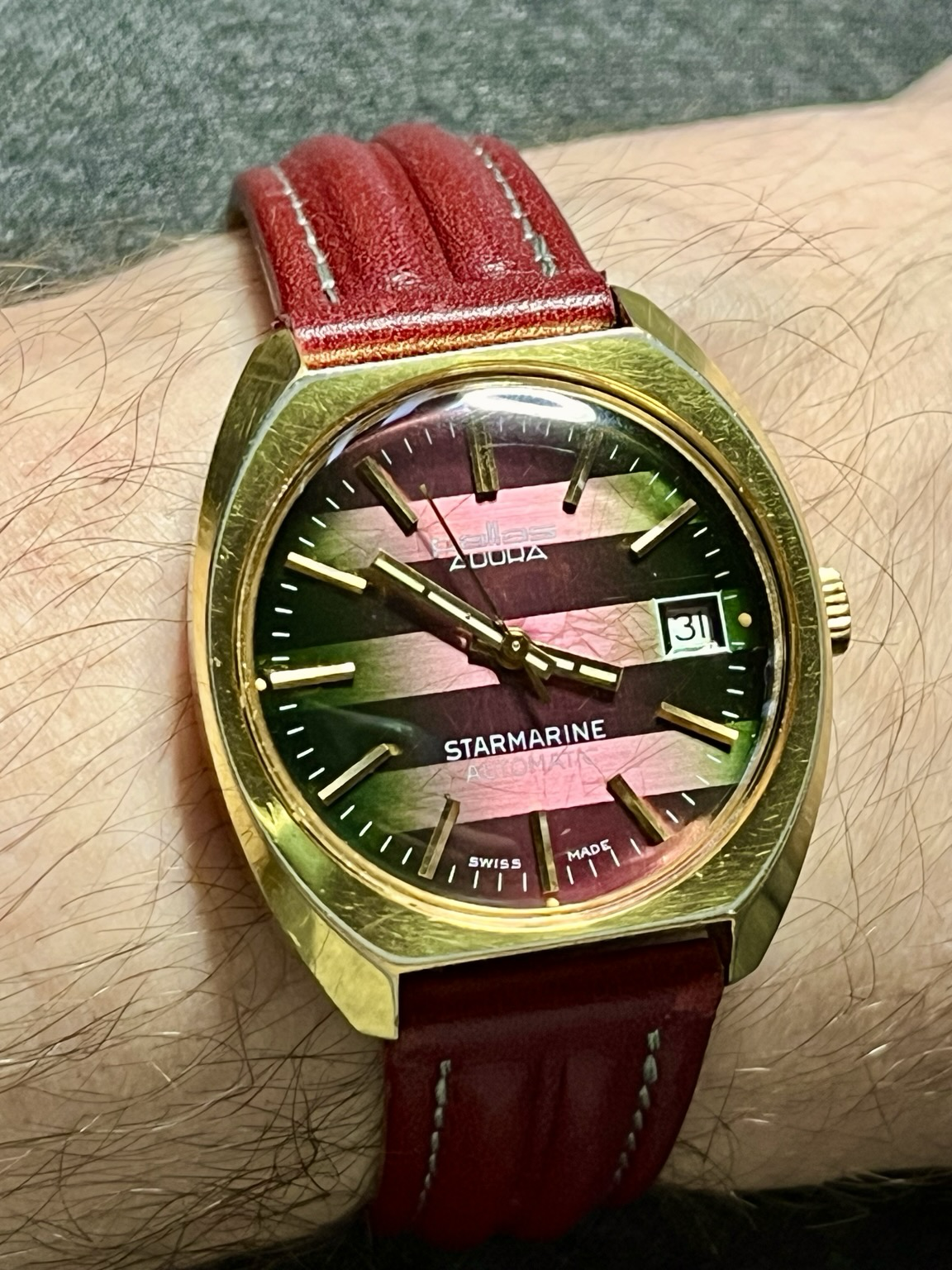 Eine goldene Armbanduhr mit einem rosa grünen Zifferblatt Eine goldene Armbanduhr mit einem rosa grünen Zifferblatt