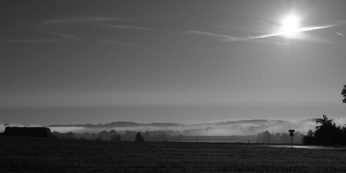 Schwarz-weiß Foto mit einem flachen Tal, aus dem helle Schwaden aufsteigen
