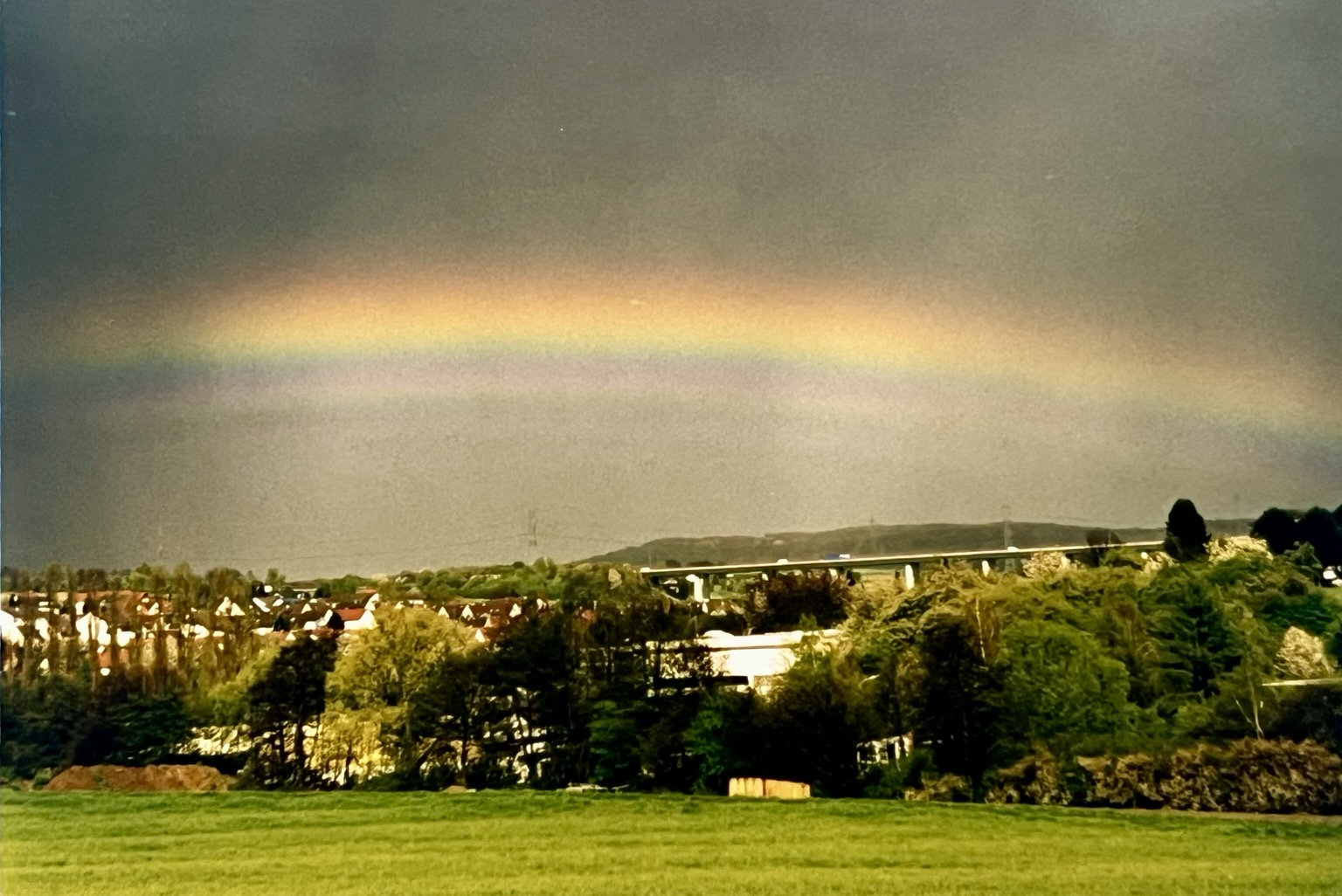 Über einen Dorf zwischen grünen Bäumen und Wiesen erstreckt sich an einen grau schwarzen Himmel ein Regenbogen Über einen Dorf zwischen grünen Bäumen und Wiesen erstreckt sich an einen grau schwarzen Himmel ein Regenbogen