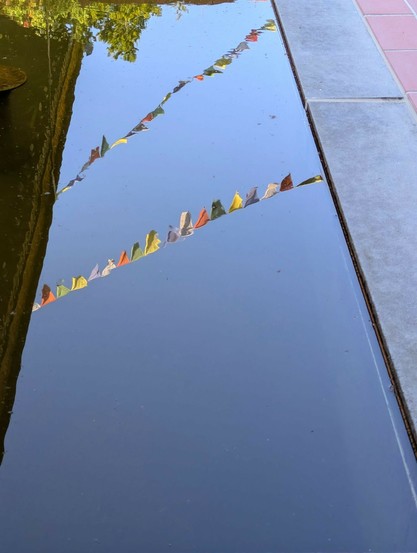 im stahlblauen Wasser spiegeln sich Gebetsfahnen