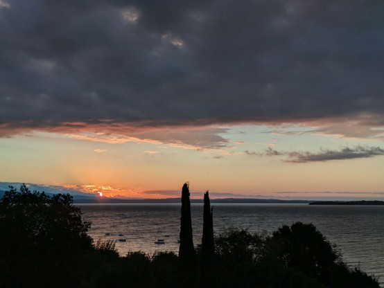 in linken Drittel erscheint ein kleiner Teil der Sonne hinter den Bergen und beleuchtet die Wolken und den See