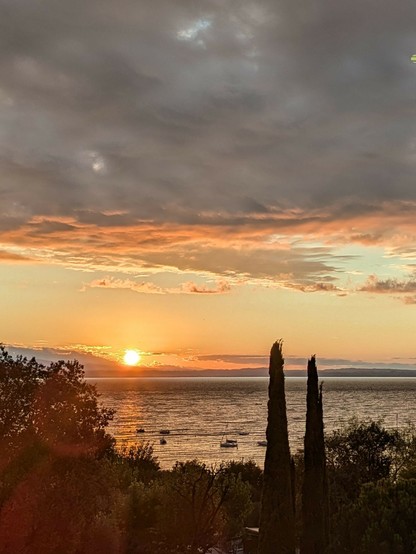 in linken Drittel erscheint die Sonne hinter den Bergen und beleuchtet die Wolken und den See