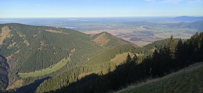 Blick von einem Berg der bayerischen Alpen in Richtung Norden ins Flache. Zwei goße Seen fügen sich in die Landschaft, Kochel und Starnberger See. der Berg vor den Seen ist mit Nadelwald bedeckt und zeicht eine unbewaldete Scharte im Teilgipfel dirikt in der Mitte des Bildes.Der Himmel ist blau, fotografiert im Herbst mit dem Tageslicht um ca 14:30 vom Laaber in Richtung Norden.