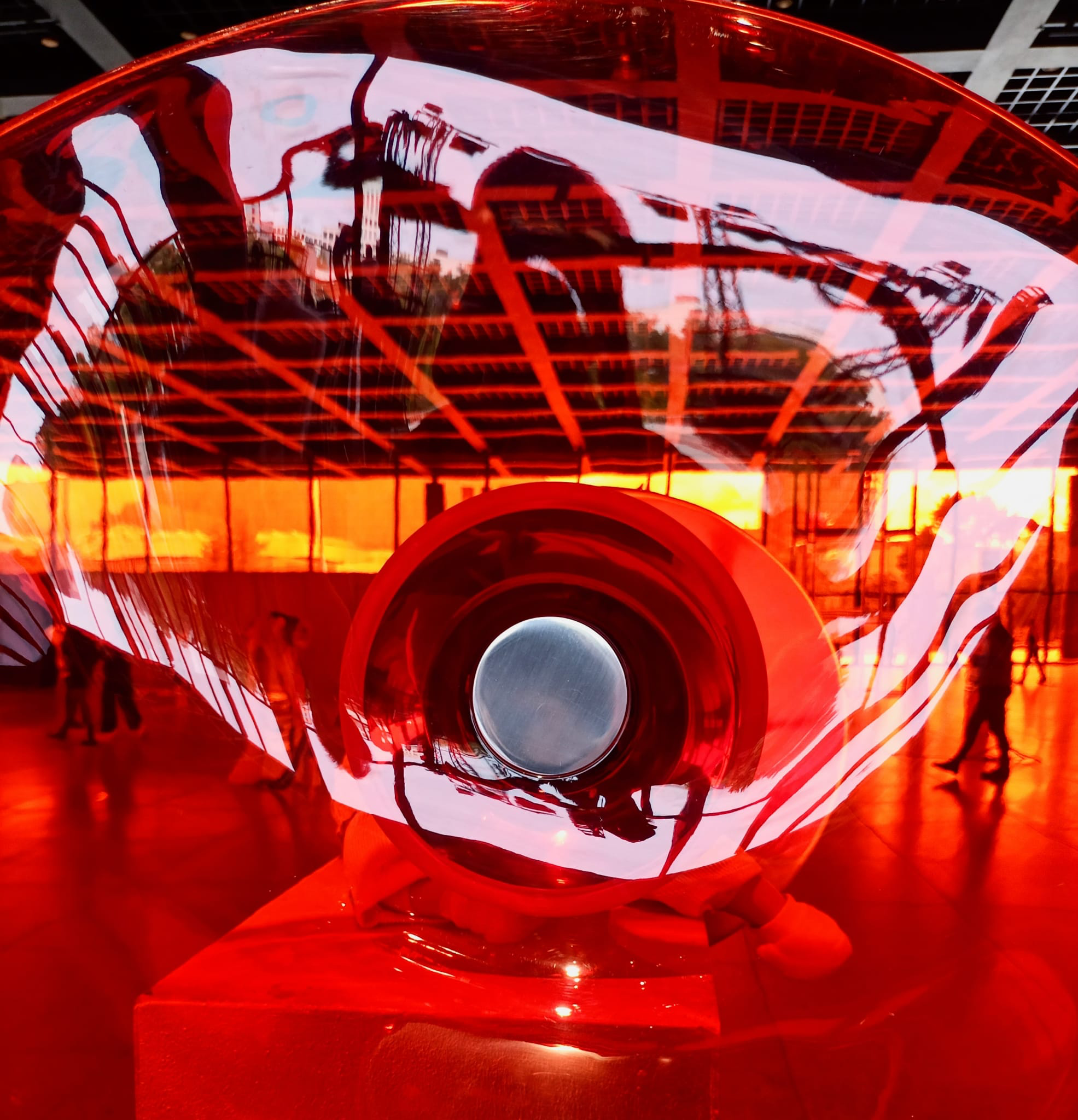 Blick durch eine rot-orangene verformte Glasfläche, dahinter sieht man die Architektur der Neuen Nationalgalerie