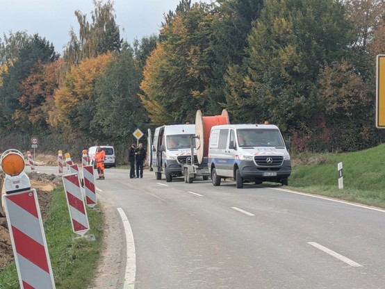 auf einer Straße stehen mehrere Kleintransporter. An einem hängt eine große Kabeltrommel