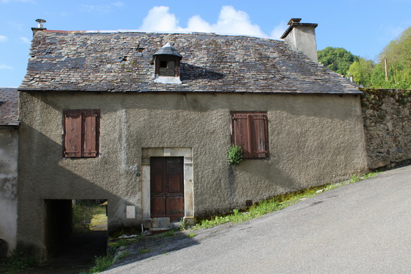altes Haus mit steinplatten gedeckt, eine kleine Gaube auf dem Dach über dem Treppenhaus. das Haus hat zwei Fenster, die mit brauchgestrichenen Fensterläden verschlossen sind. Die Wohnung mit den zwei Fenstern liegt im Hochpaterre. Die Haustür aus Holz ist dunkelbraunund mit den Laibungen und Sturz in Stein ausgeführt. das Haus ist alt, anscheinend unbewohnt, der Putz grau. Unter dem linken Fenster ist eine Duchfahrt in den Innenhof.