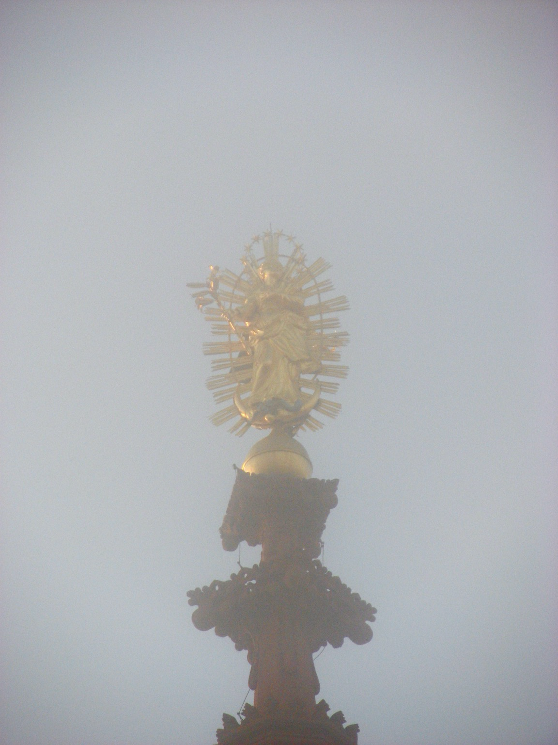 Durch Nebel hindurch sieht man eine goldene Statue auf einer braunen Kirchturms spitze