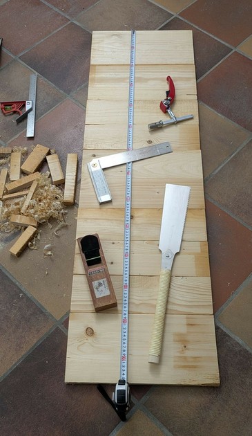 auf gleich langeb Brettern liegt ein Maßband, eine japanische Säge, ein japanischer Hobel, ein klappbarer schwedischer rechter Winkel und ein Niederhalter für eine Hobelbank
