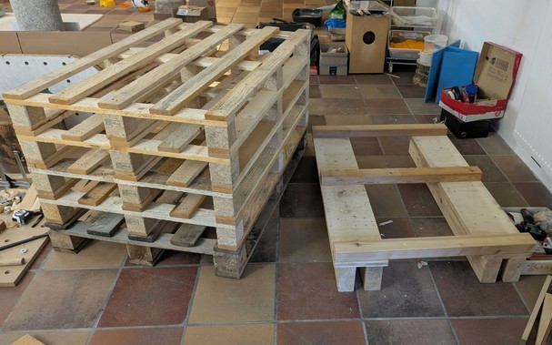 5 übereinander liegende verschraubte Paletten und daneben weiteres Holz für den Unterbau