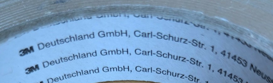 Foto einer Kleberolle, auf der Innenseite steht wiederholt:
3M Deutschland GmbH, gefolgt von einer Adresse. Das 3M ist als Logo mit anderer Schrift und setzt sich dadurch ab, so dass man den Text ab Deutschland GmbH als Text wahrnimmt.
