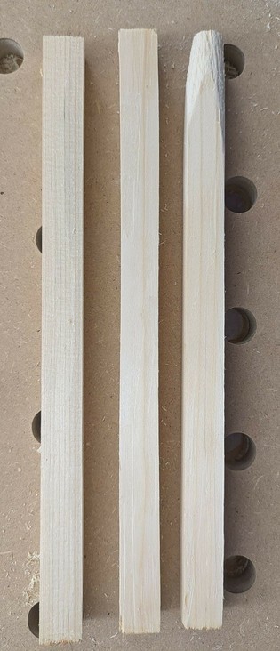 drei quadratische längliche Hölzer liegen auf einer hölzernen Lochplatte. eins ist konisch angeschnitten