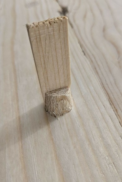 ein Zapfen schaut durch eine Holzfläche und ein Keil steckt senkrecht in dem Zapfen