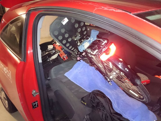 offene Beifahrertür, und auf dem flach gelegten Beifahrersitz ist ein Hinterrad und Sitz vom Liegerad erkennbar