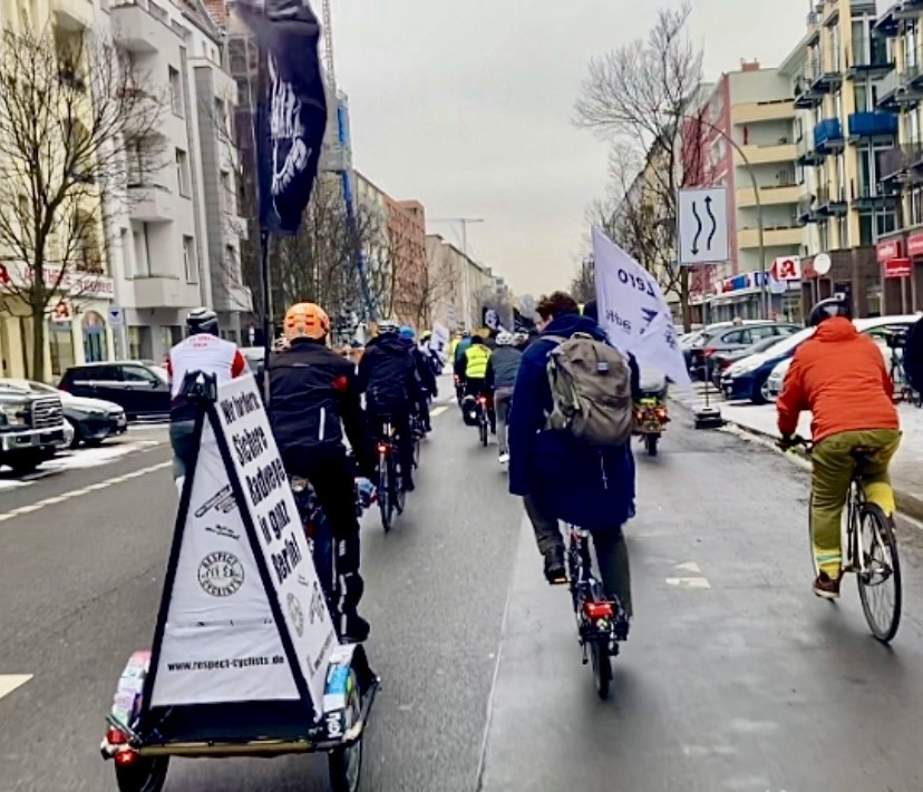 Teilnehmende einer VisionZero Fahrraddemo fahren auf der Fahrbahn einer Berliner Hauptverkehrsstraße. Es sind Fahnen des ADFC Berlin und RespectCyclists zu sehen.