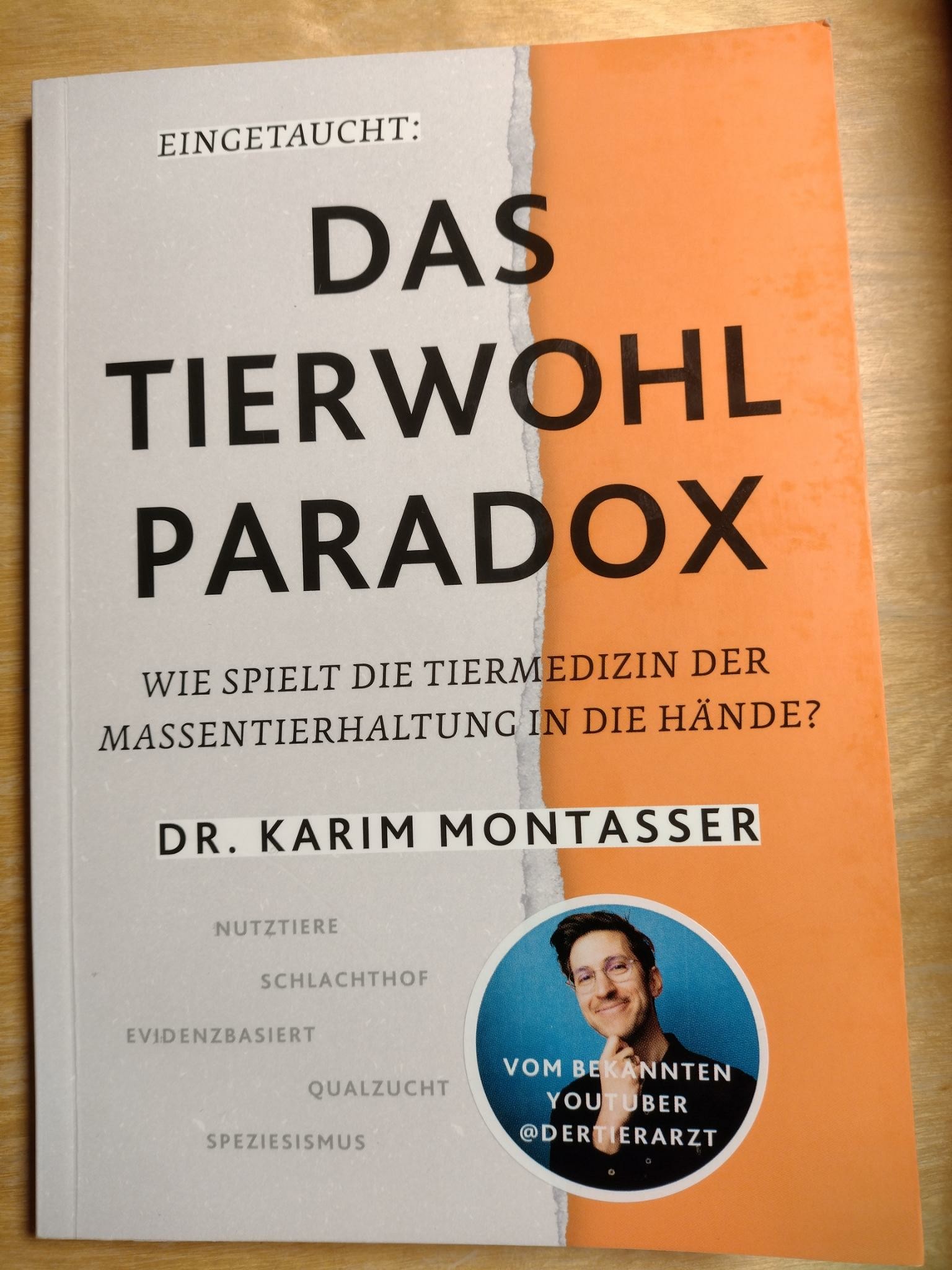 Ein Buch auf einem Tisch mit dem Titel Das Tierwohl Paradox - Wie spielt die Tiermedizin der Massentierhaltung in die Hände? vom Dr. Karim Montasser.