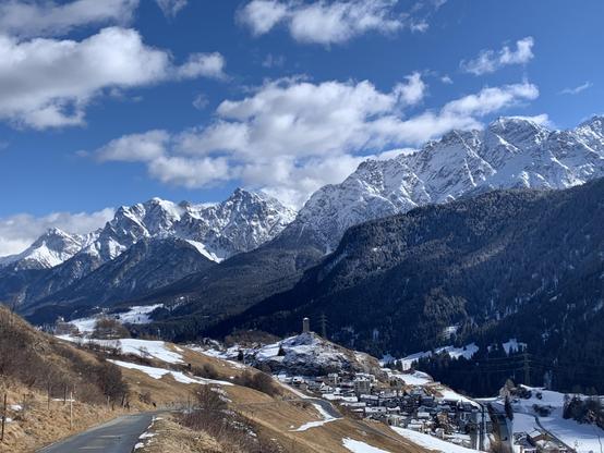 Aussicht talabwärts. Links erkennt man vielleicht das Schloss Tarasp, in der Mitte Ardez mit der Ruine Steinsberg. Der Himmel leicht verhangen, die Hänge auf der rechten Schattenseite schneebedeckt, auf unserer linken Sonnenseite deutlich mehr braun. Hinten die sehr schroffen Berge.