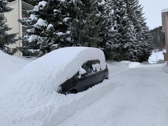 Ein Auto mit etwa 30 cm Neuschnee auf dem Dach. Der Hauswart hat den Schnee auf dem Weg fein sauber dem Auto entlang weggefräst.