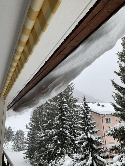 Blick auf die Dachunterseite. Der Schnee quillt über die Dachkante und ist im Begriff, abzufallen.