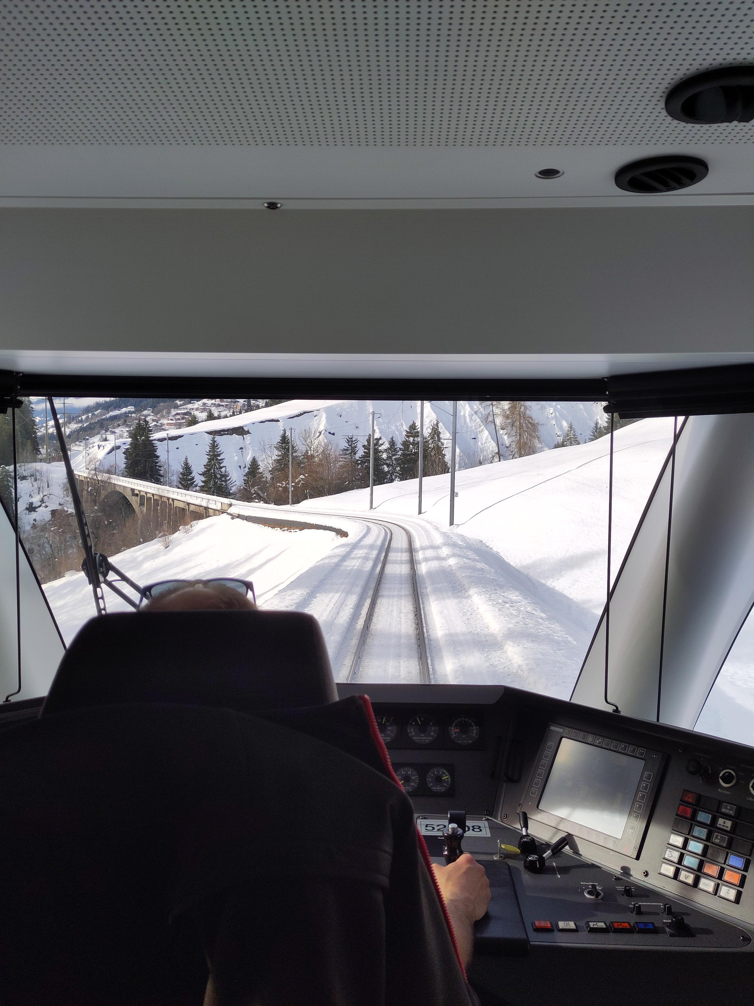 Foto. Blick durch einen Führerstand auf eine Eisenbahnbrücke im Schnee.