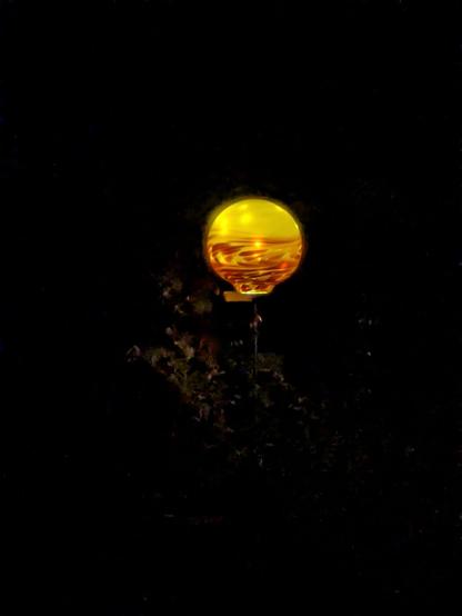 eine von innen beleuchtete gelborange Glaskugel in der Nacht 
