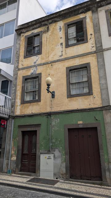 Ungewohntes Haus, Putz und Farbe an Teilen abgeblättert. Im Hochparterre und 1. Stoch jeweils zwei Fenster, bei denen die untere Hälfte zu Öffnen nach oben geschoben werden kann. Die Fensteteile sind mit Holzrahmen nochmal in sechs Einzelgläser unterteilt. Putz des Hauses in Ocker, Erdgeschoss schwarzes Lavagestein.