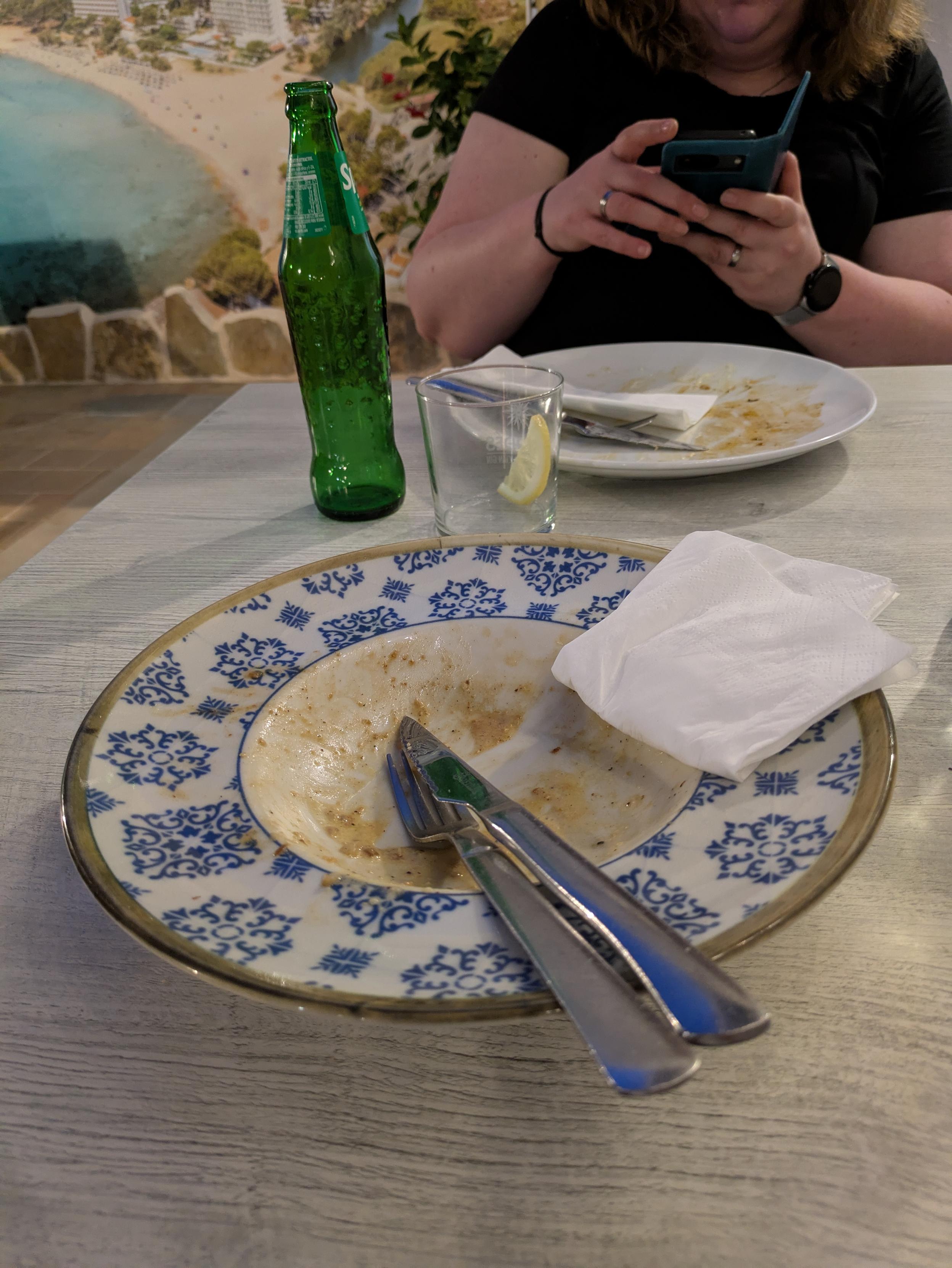 Ein Foto. Eine Person sitzt an einem Tisch vor zwei leeren Tellern