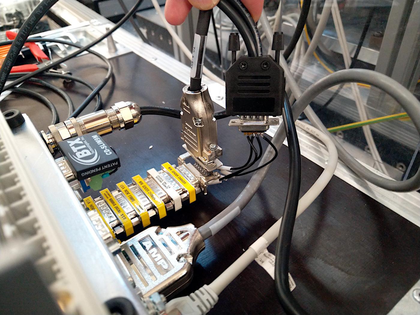 Foto von einer sehr experimentellen, äh, „Verkabelung“.

Von einem Controller (unten links, im Foto aber verdeckt) müssen elektronische Signale über einen Y-Adapter abgegriffen werden. Aus Gründen wurde ein 90° gewinkelter Adapter mit Steckkontakten auf einer und Aufnahmekontakten auf der anderen (traditionell als „männlich“ und „weiblich“ benannt) Seite genutzt, also 1:1 durchkontaktiert; hier wurden dann die vier benötigten Signale über (sehr) kurze Adern mittels Lötkontakt abgegriffen und auf einen 9-poligen Stecker gegeben; von diesem geht es per bestehendem Kabel zu einem FPGA (das Gehäuse ragt links ganz leicht ins Bild rein).

Beim Anschließen zeigte sich, dass der 90°-Winkel zu zwei Problemen führt:
– Der Stecker geht nach unten weg, setzt auf dem Tisch auf; Lösung: Controller umdrehen, jetzt geht der Stecker nach oben, da ist Platz.
– Der Stecker trifft auf einen anderen Stecker (ein schwarzes Dings mit „BTX“ beschriftet im Bild: eine kleine Interlock-Schaltung welche auf „immer an“ gescchaltet ist; hiermit ließe sich der Betrieb des Motors etwa über Sicherheitsschalter deaktivieren) und kommt nicht dran vorbei.
„Lösung“: eine Reihe alternierender Gender-Adapter, um den Stecker weit weg vom Gehäuse zu führen.
