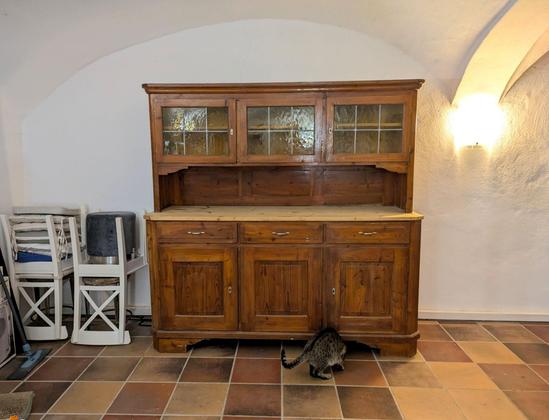 ein altes hölzernes Küchenbuffet steht im Bogen von einem Gewölbe. Ein getigerter Kater davor