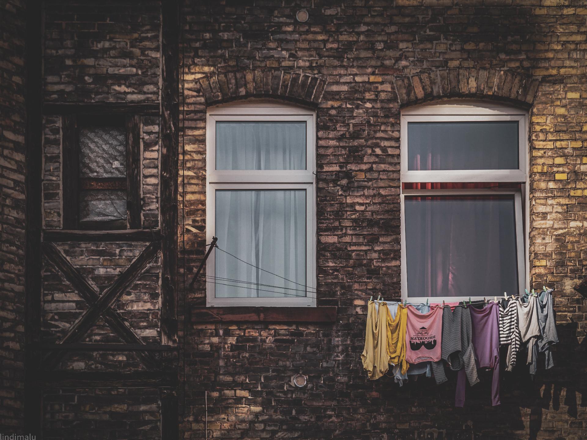 Zwei Fenster in einer Backsteinfassade, an einem Fenster hängt Wäsche zum Trocknen an der Leine.