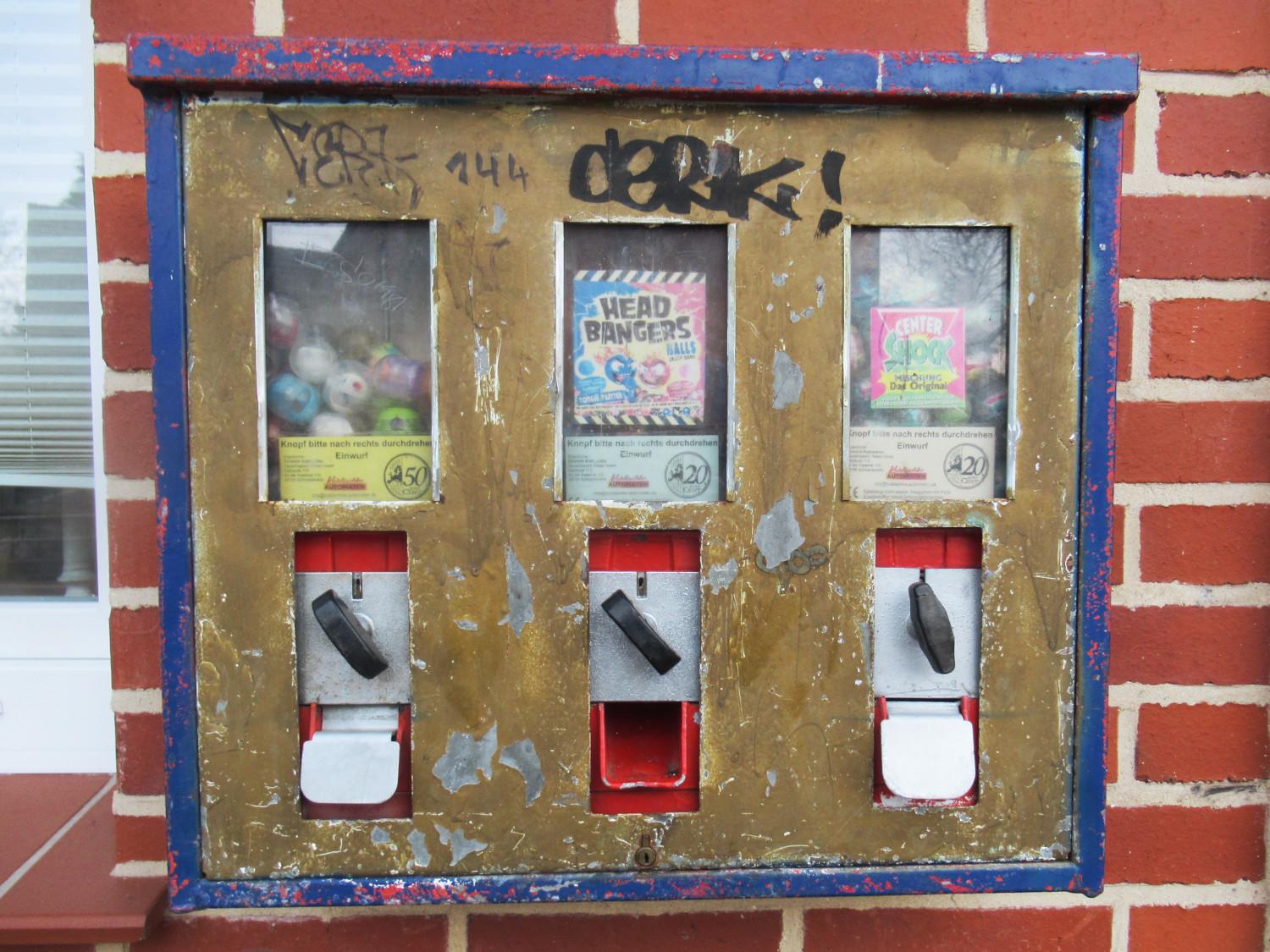 Ein in die Jahre gekommener Kaugummiautomat an einer roten Klinkerfassade