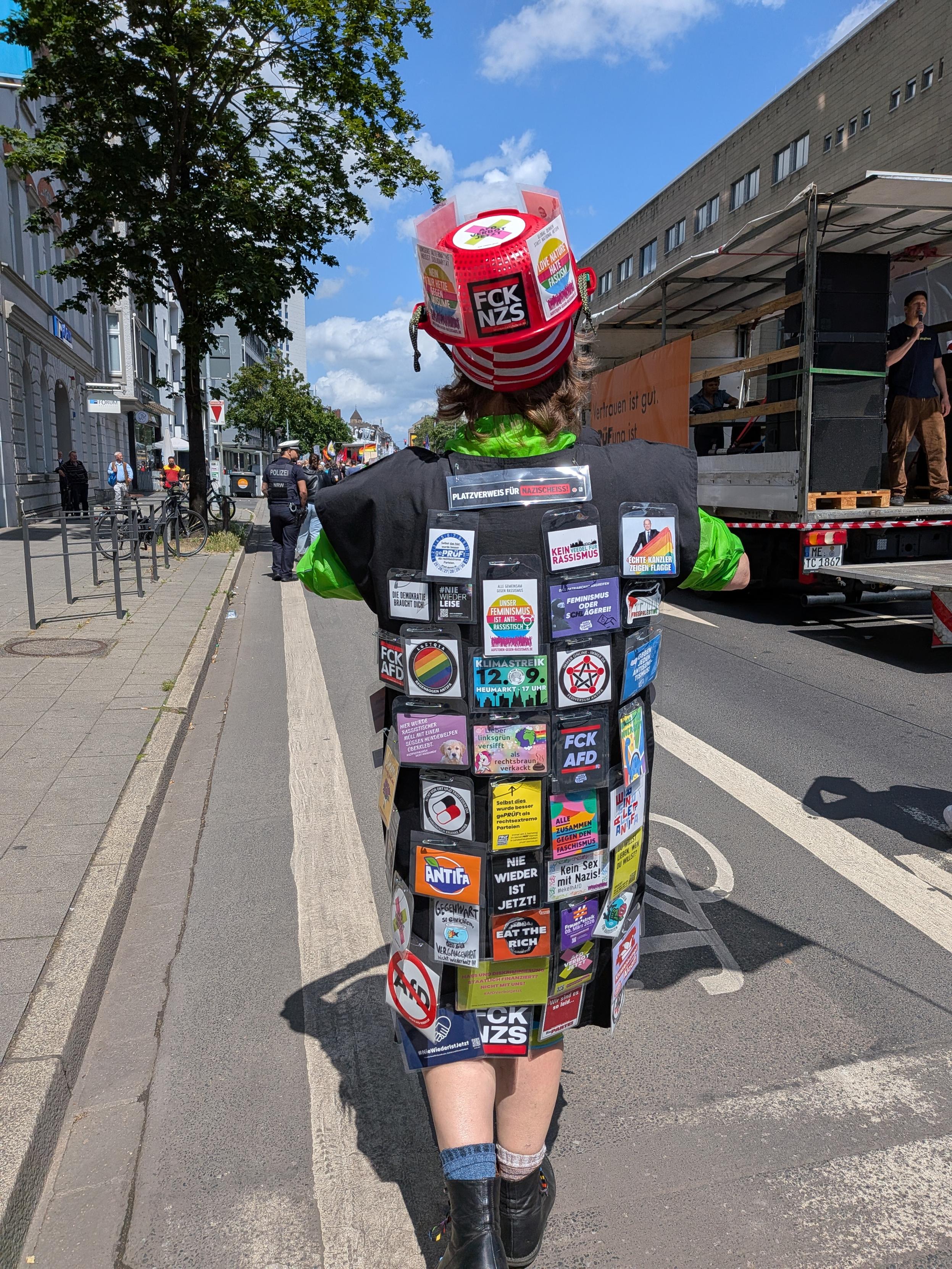 Person von hinter fotografiert in Kutte, mit diversen anti Faschismus Anstecker
