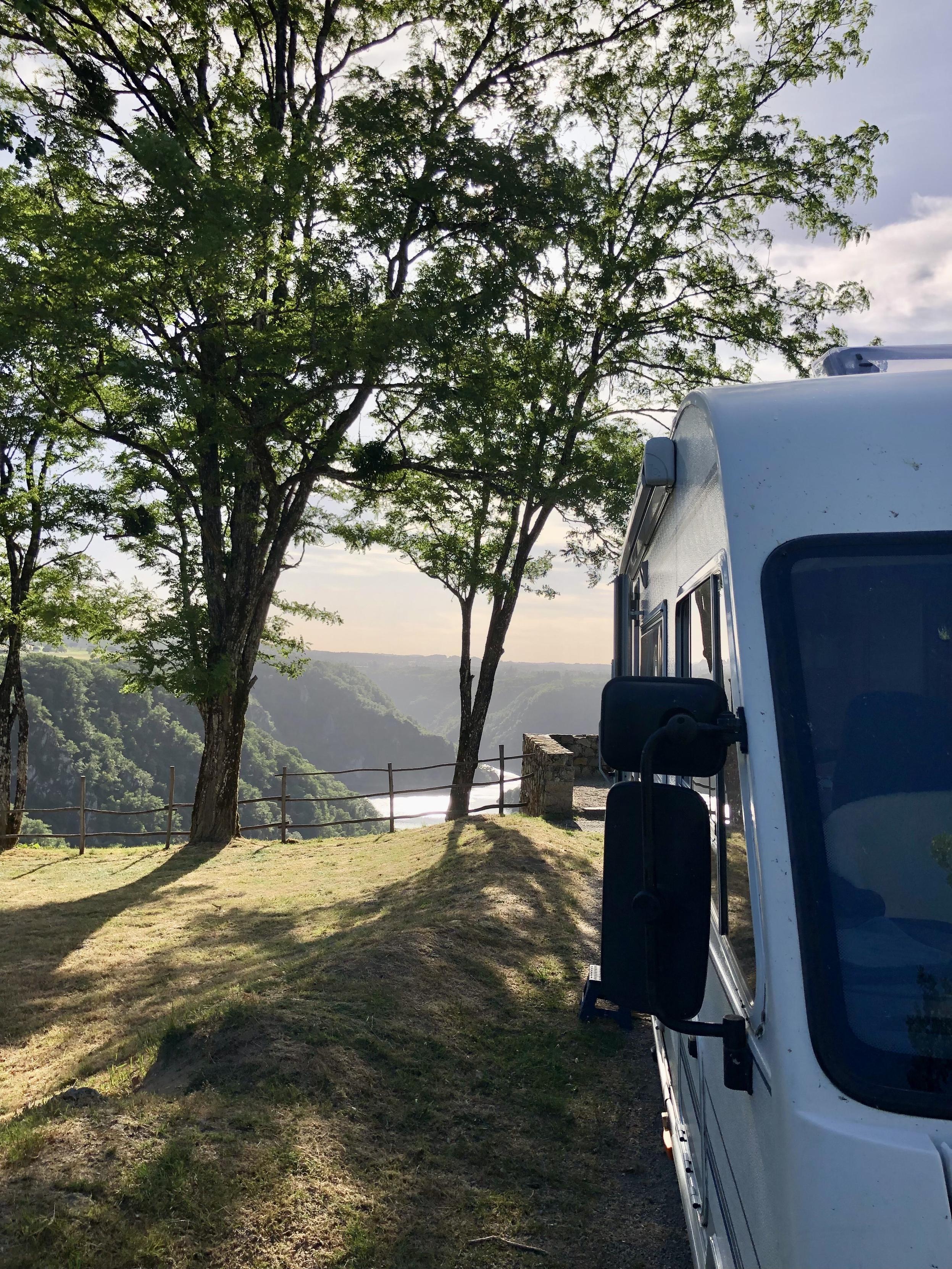 Teile eines Wohnmobils von vorne. Dahinter Bäume und der Blick ins tiefe Flusstal.
