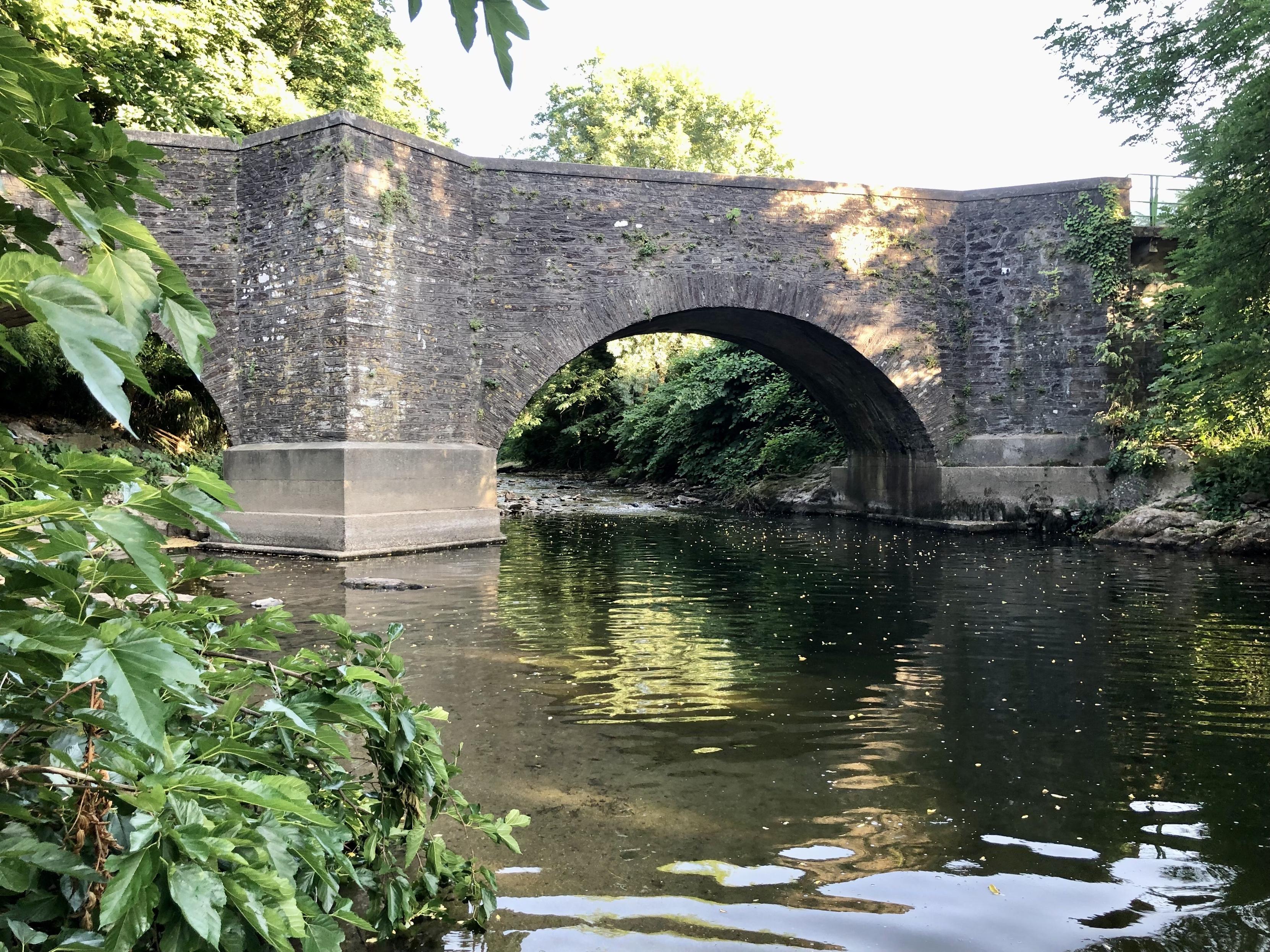 Steinerne Bogenbrücke, die einen kleinen Fluss überspannt. Fotografiert vom Fluss aus.