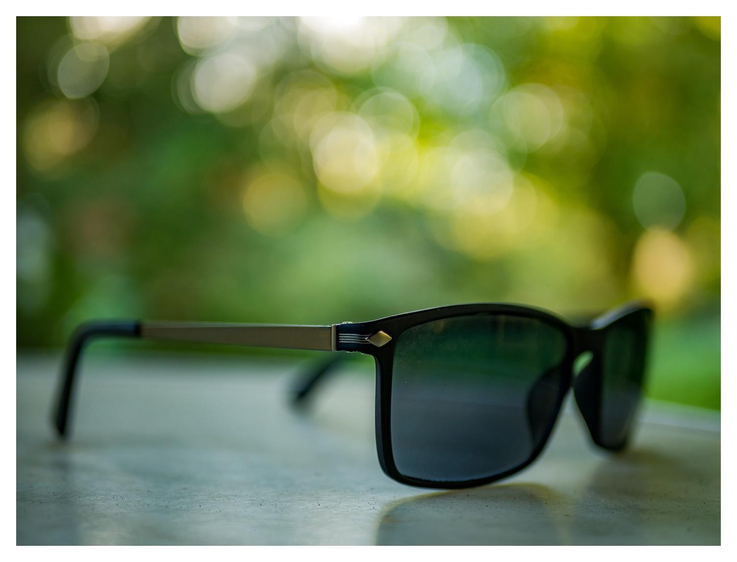 Sonnenbrille auf einem Tisch im freien. Im Hintergrund grüne Bokeh Bubbles